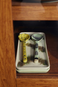 Two ceramic ladles on a rectangular plate with a wooden background