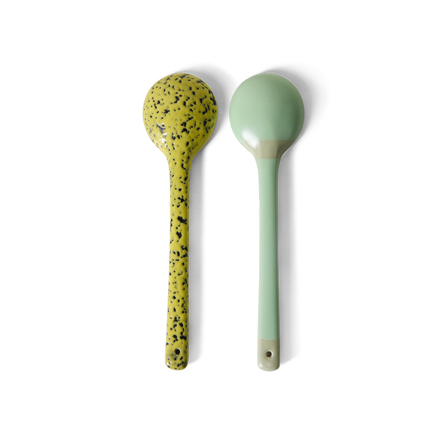 Two spoons, one yellow with black speckles and one green, on a white background
