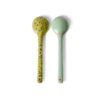 Two spoons, one yellow with black speckles and one green, on a white background