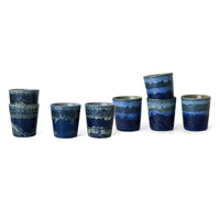 Set of eight blue ceramic cups with wave patterns on a white background