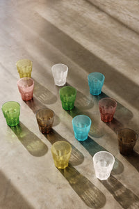 Colorful glass tumblers arranged on a textured surface with shadows.