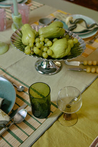 Decorative table setting with fruit bowl, glasses, and cutlery on a checkered tablecloth.