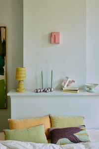 Decorative headboard with colorful pillows and a small shelf with items against a light blue wall.
