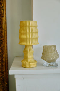 Yellow textured lamp and glass vase on a white surface with a decorative mirror in the background.