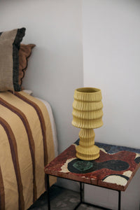 Yellow textured vase on a decorative side table next to a bed with striped bedding.