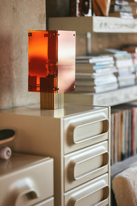 Decorative orange glass vase on a shelf with books and a mirror in the background
