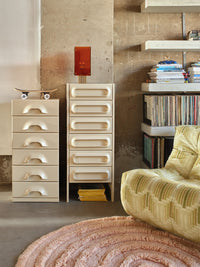 Beige dresser with multiple drawers in a room with a textured wall and a chair.