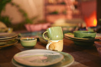 Dining table with green ceramic dishes and cups in a warm, indoor setting.