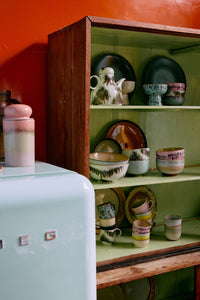 Vintage-style kitchen with a retro refrigerator and wooden shelf displaying ceramic items against an orange wall.