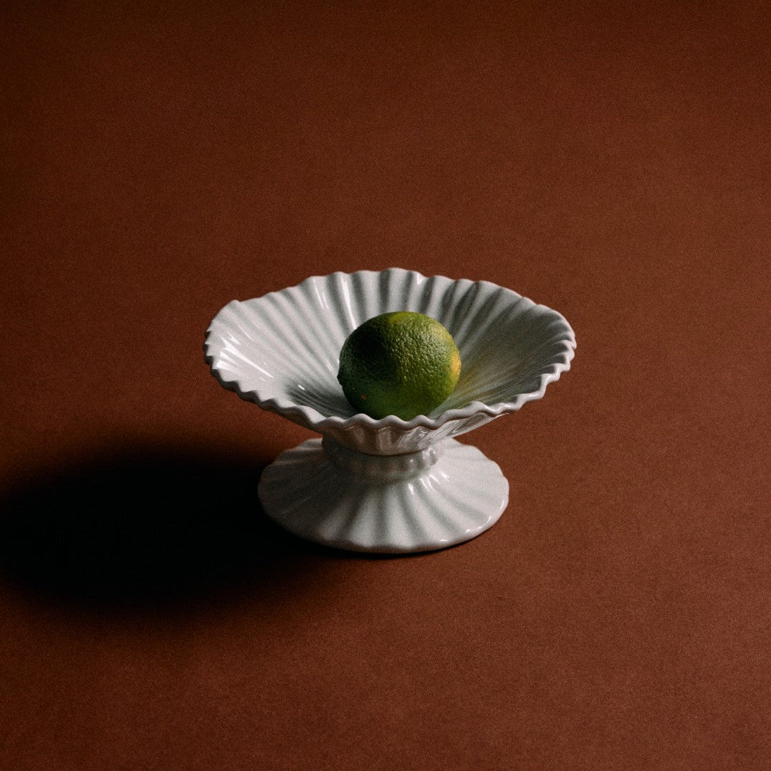 White decorative bowl with a green fruit on a brown background