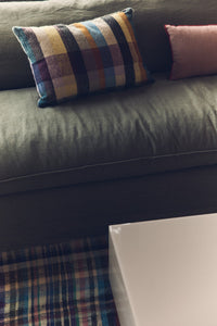 Gray sofa with colorful plaid pillow and pink cushion on a checkered floor.
