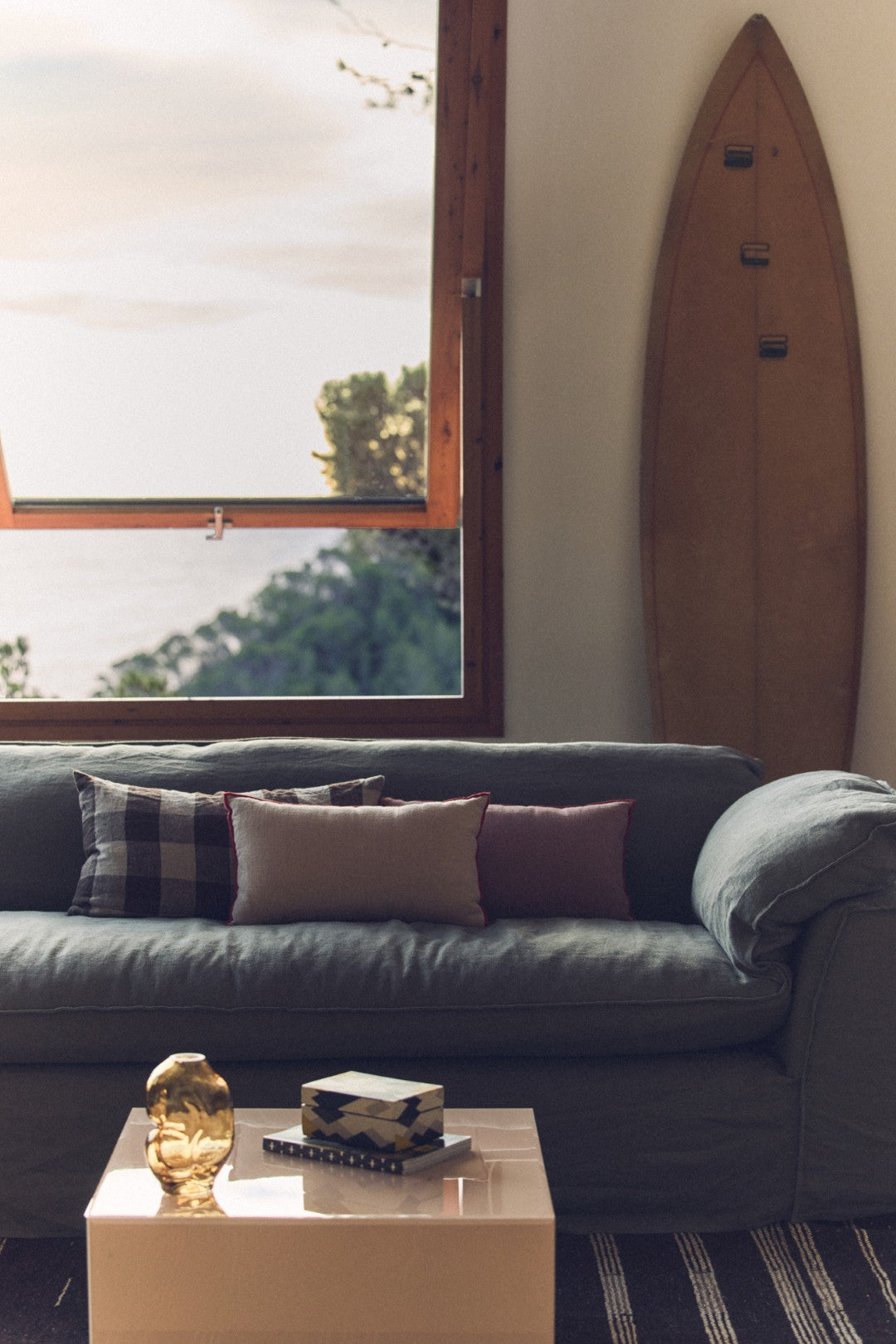 Living room with a gray sofa, coffee table, and surfboard on the wall.