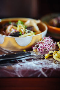 Close-up of a bowl of pasta with various toppings on a wooden table.