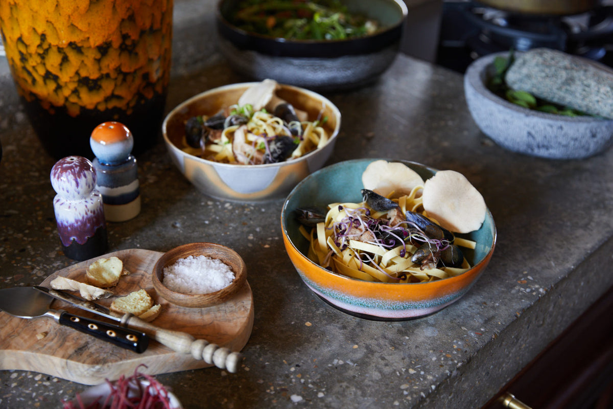 Dishes of food on a stone surface with various seasonings and a knife.