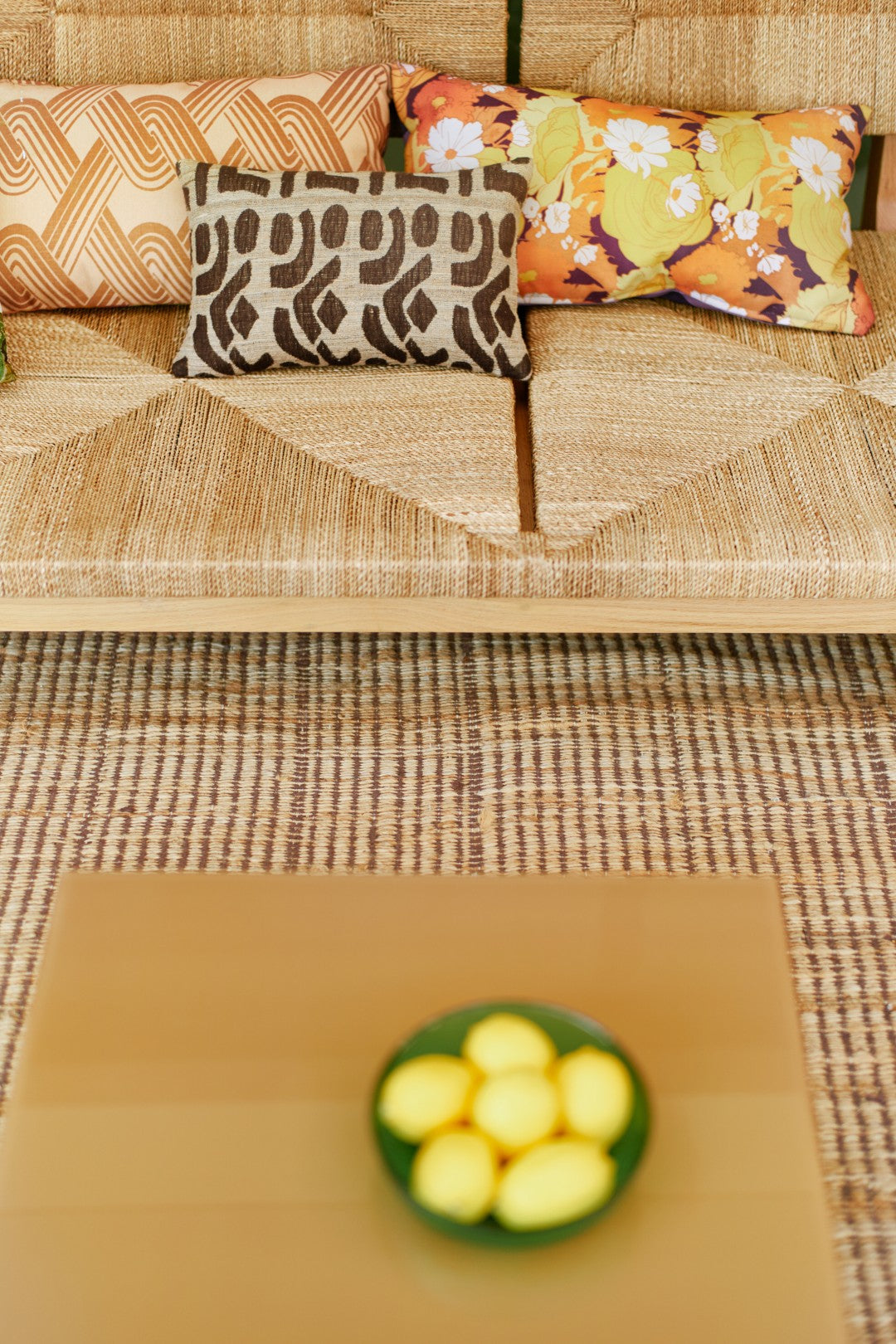 Decorative pillows on a textured sofa with a glass bowl of lemons on a wooden table in front.