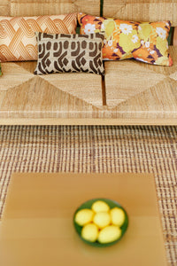 Decorative pillows on a textured sofa with a glass bowl of lemons on a wooden table in front.