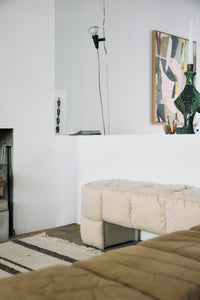 off white upholstered bench against wall with painting in background