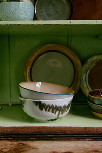 Stack of ceramic bowls with green and brown patterns on a wooden shelf.