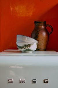Ceramic bowls and a pitcher on a Smeg appliance against an orange wall.