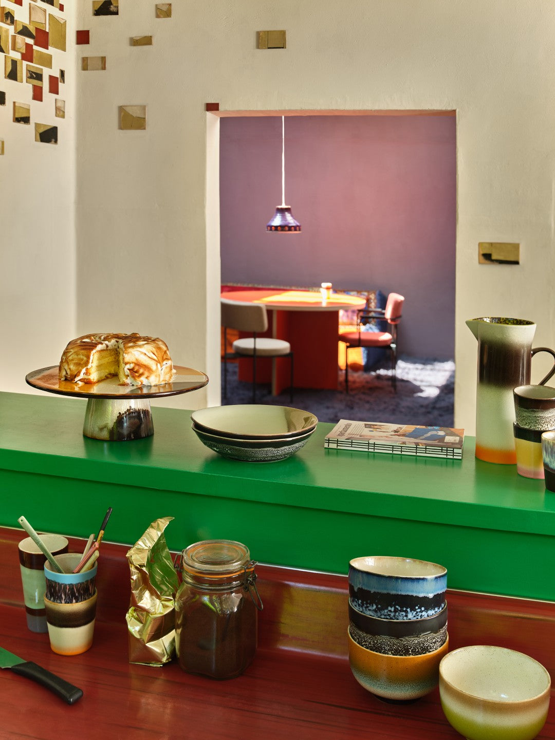 Dining area with a green counter, colorful tableware, and a mirror reflecting the room.