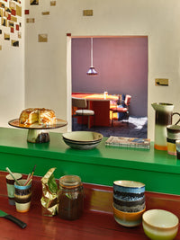 Dining area with a green counter, colorful tableware, and a mirror reflecting the room.