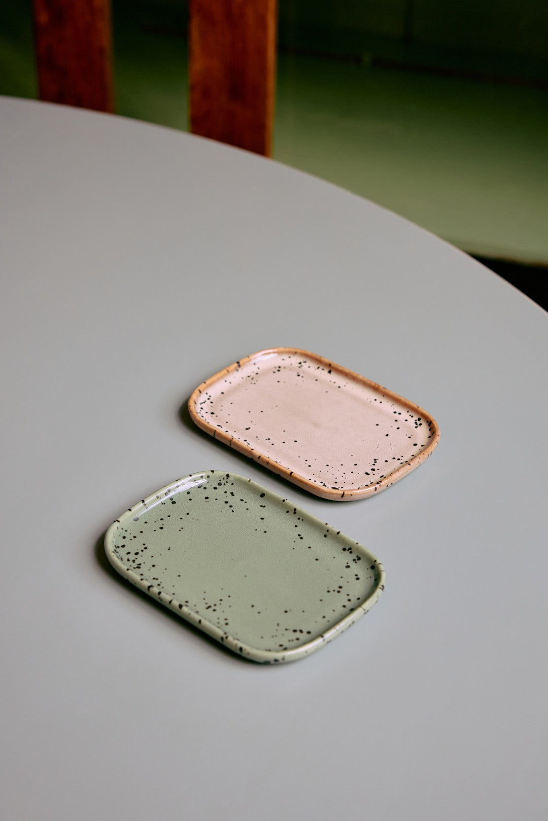 Two ceramic coasters, one green and one pink, on a gray surface.
