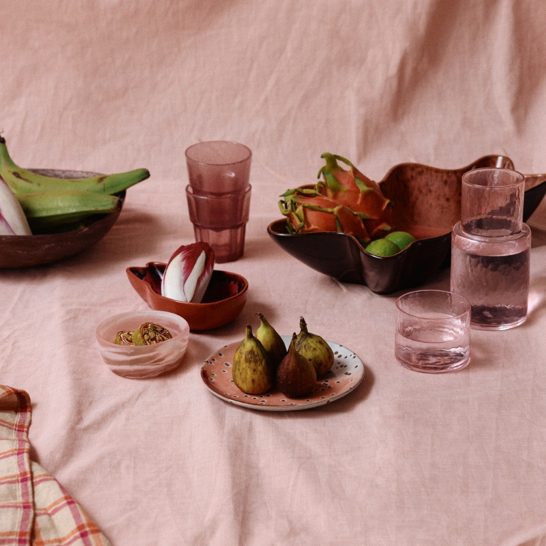 Table setting with fruits, glasses, and a plaid cloth on a pink fabric background
