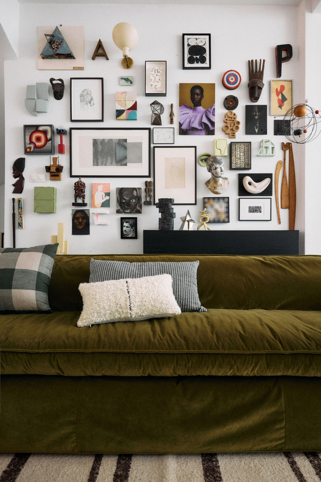 Green sofa with decorative pillows in a room with a wall of framed art and sculptures.