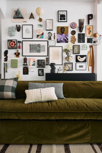Green sofa with decorative pillows in a room with a wall of framed art and sculptures.