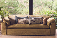 Green sofa with patterned cushions in a room with large windows and greenery outside