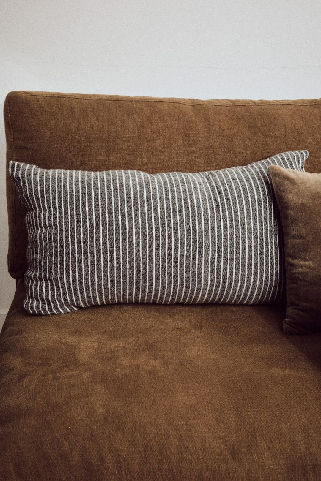 Brown sofa with a striped gray pillow on a plain background