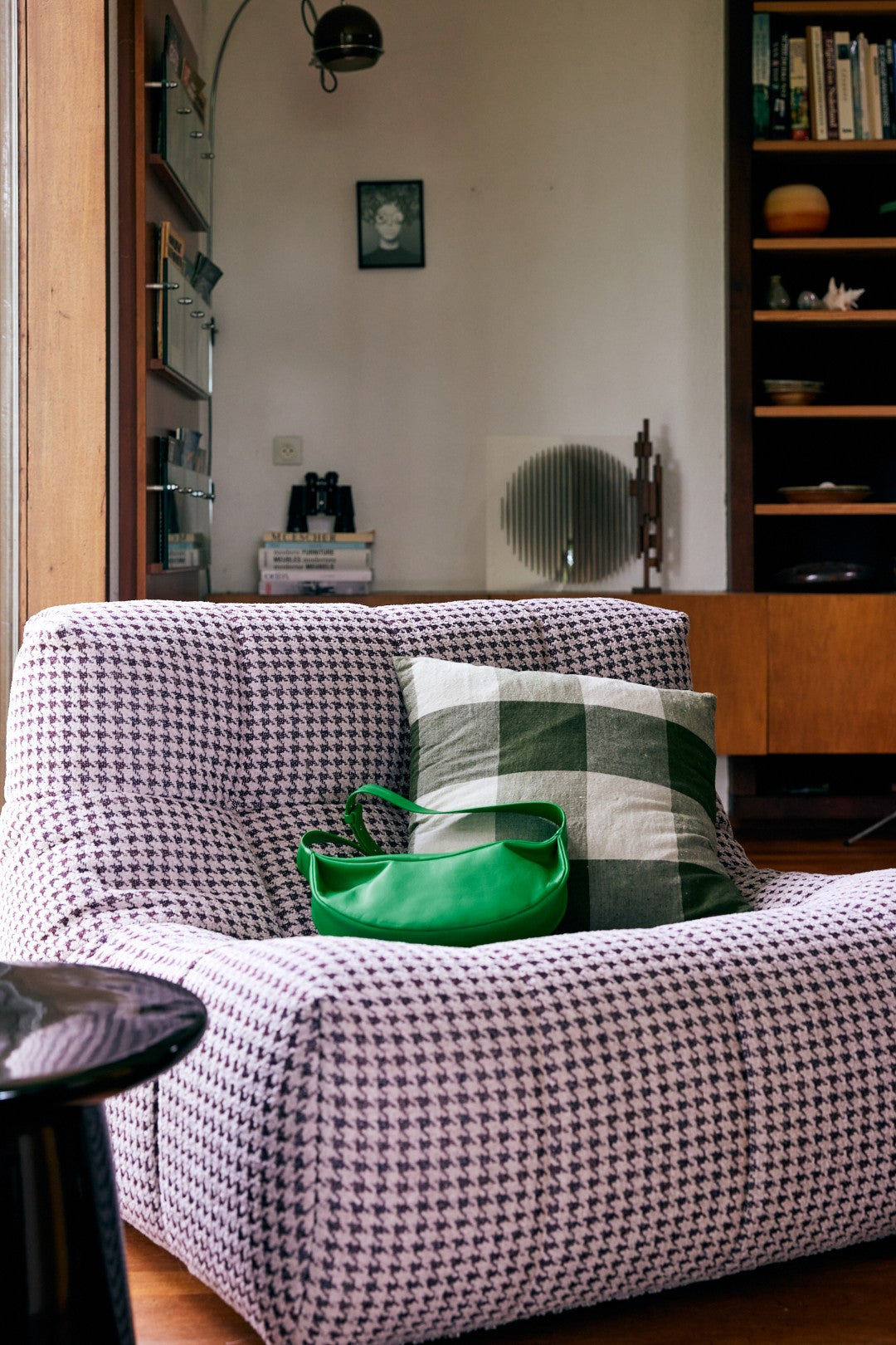 Checkered sofa with a green bag and plaid pillow in a room with shelves and decor.