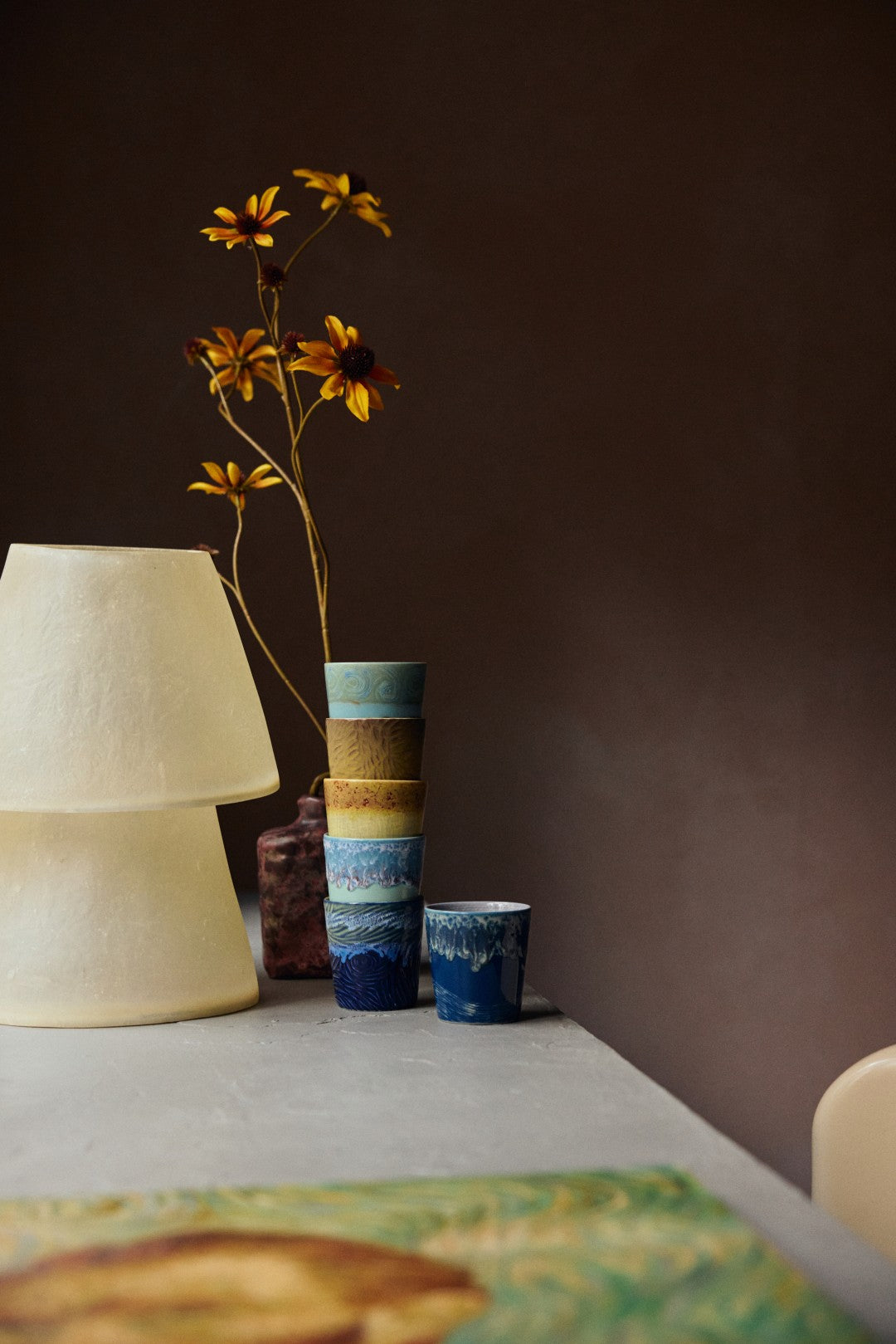 Stack of colorful ceramic vases with a single flower on a table against a dark wall.