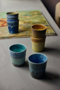 Stacked ceramic cups with blue and green glaze on a textured surface