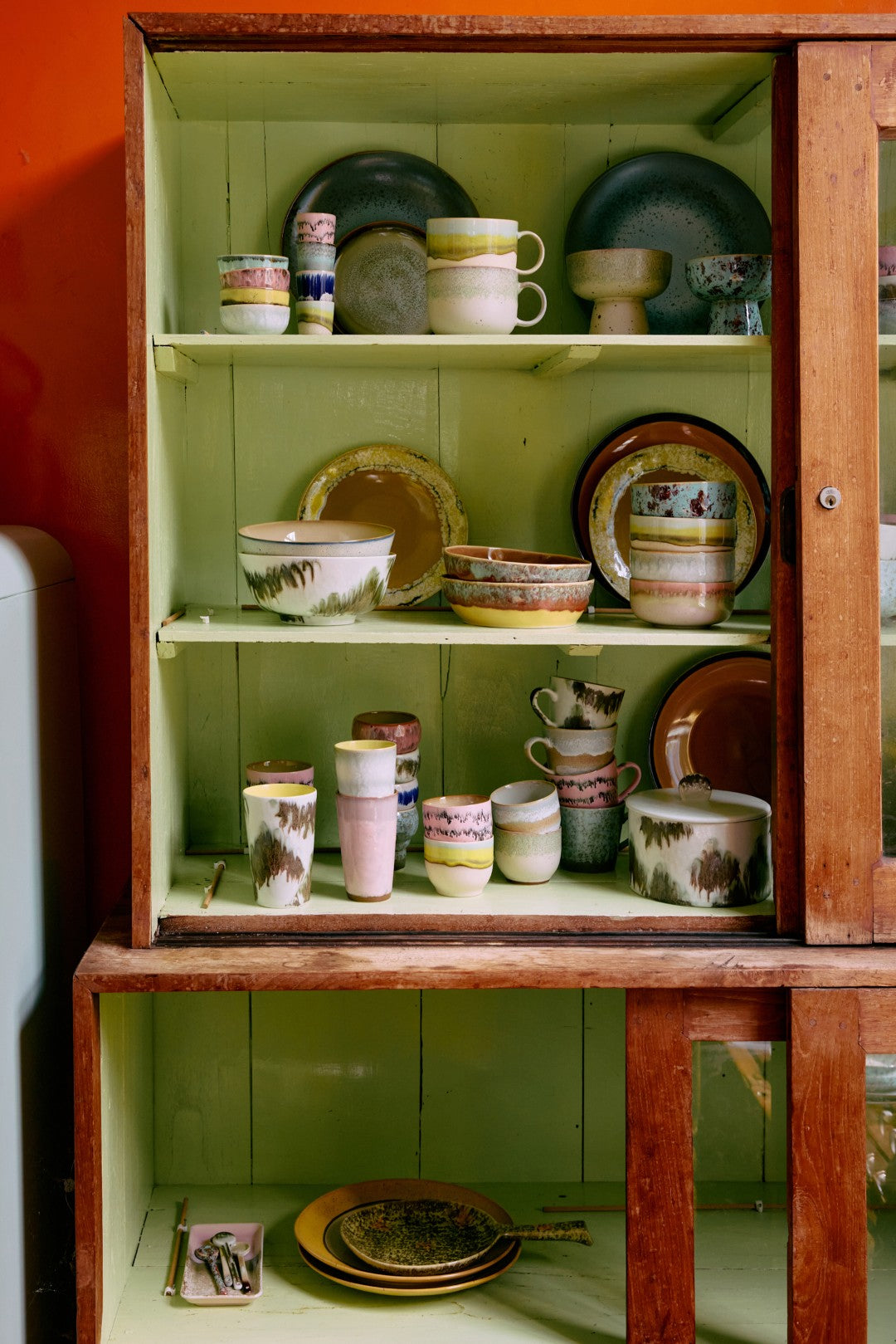 Wooden cabinet with ceramic dishes inside against a green wall.