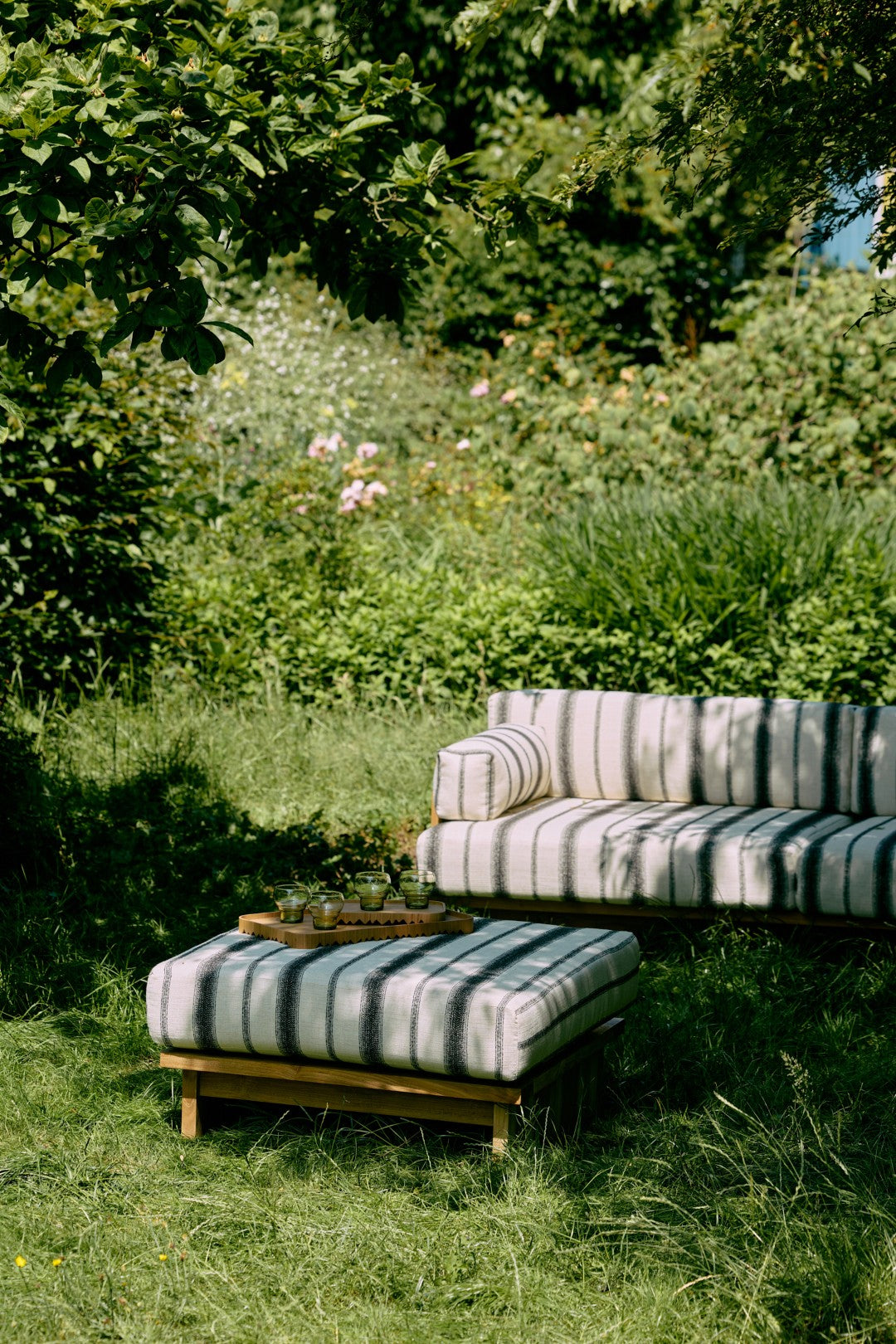 Striped outdoor sofa and ottoman in a garden setting with greenery.