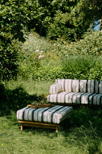 Striped outdoor sofa and ottoman in a garden setting with greenery.