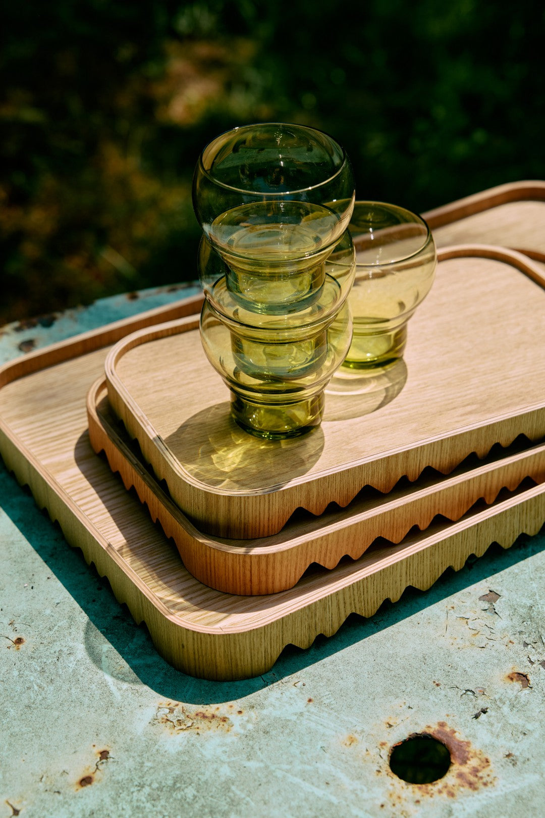 Three stacked glass tumblers on a wooden tray with a natural outdoor background