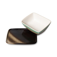 Two square ceramic dishes, one black and one beige with a greenish tint, on a white background.