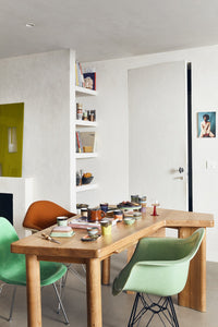 Modern dining area with wooden table and green chairs, bookshelf in the background