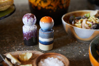 Two ceramic salt and pepper shakers on a kitchen counter with food items in the background.
