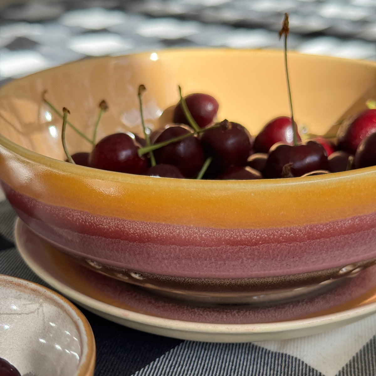 Cherries in a ceramic bowl on a checkered fabric background