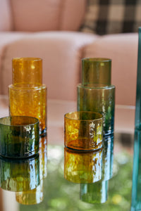 Set of multicolored glass tumblers on a reflective surface with a blurred background