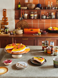 Dessert display on a kitchen counter with a cake and pastries, surrounded by kitchenware.