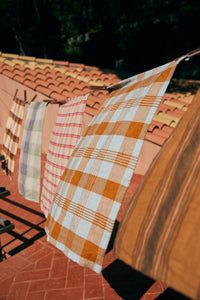 Plaid and striped cloths hanging on a clothesline against a tiled roof.