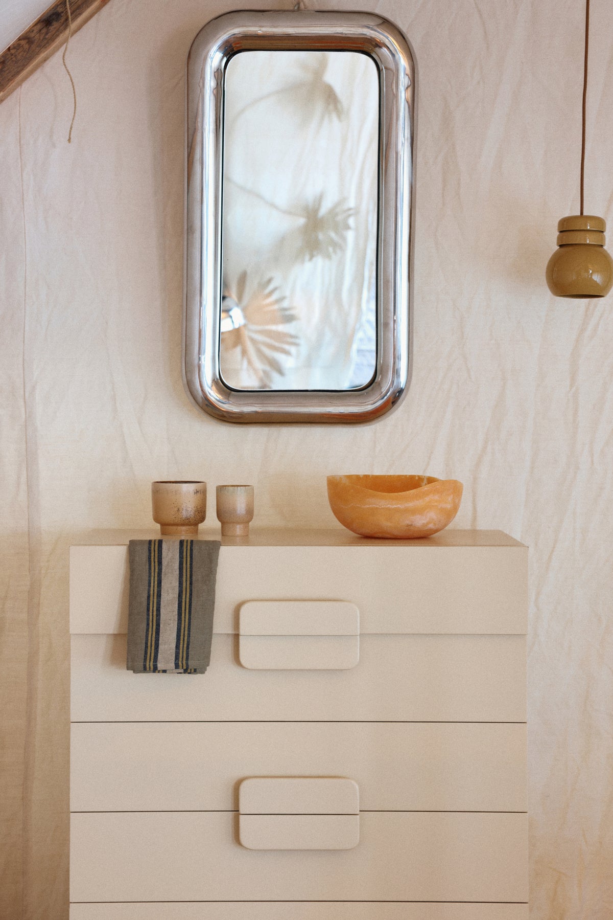 Beige dresser with decorative items and a mirror on a light wood wall.