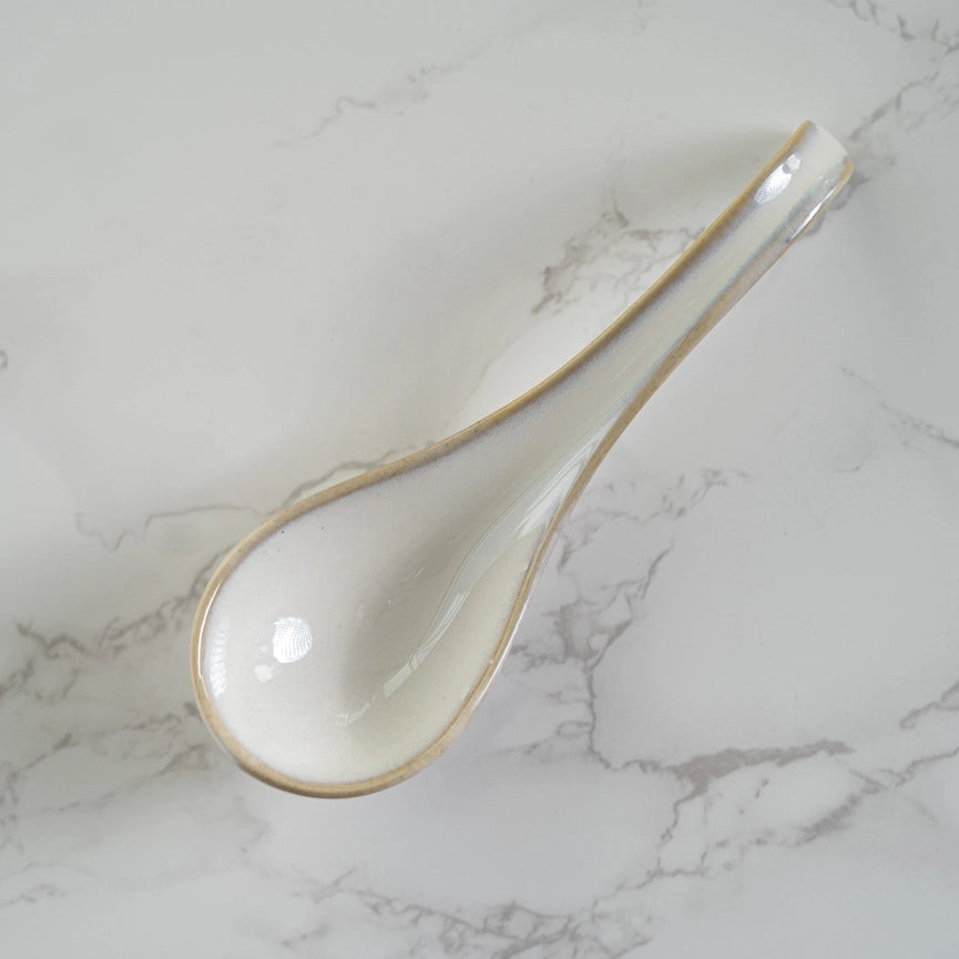 White ceramic spoon with gold rim on a marble surface