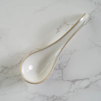 White ceramic spoon with gold rim on a marble surface