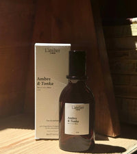L'atelier Ambre & Tonka perfume bottle and packaging on a wooden surface.