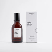 Brown perfume bottle with black cap and white label next to a white box labeled 'Ambre & Tonka' on a light gray background.